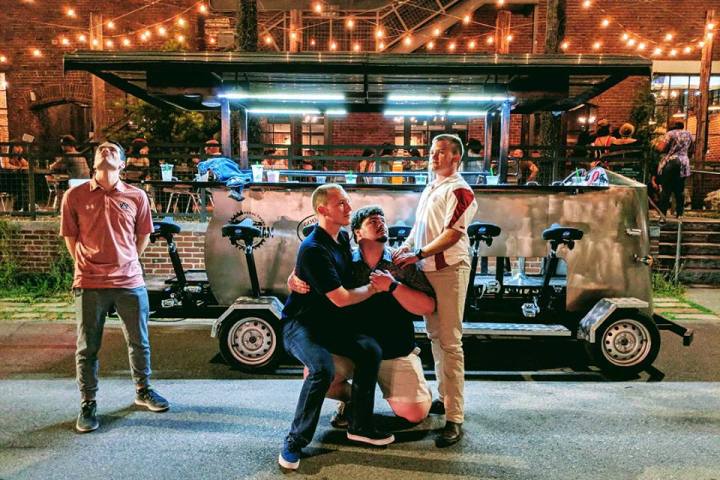 Three men posing in front of Hawaiian-themed party pedal bike